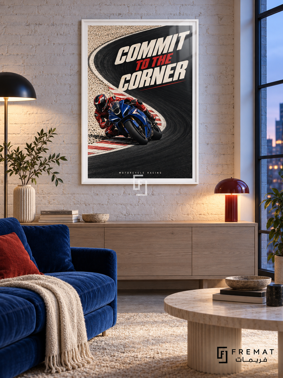 Commit To The Corner: A blue motorcycle and red-suited rider lean into a sweeping black track corner bordered by cream ground and red accents. White frame with a white printed border, displayed in a styled room.