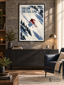 Follow The Fall Line: A skier in red carves across ivory snow with parallel tracks and diagonal navy shadows. Black frame with a white printed border, displayed in a styled room.