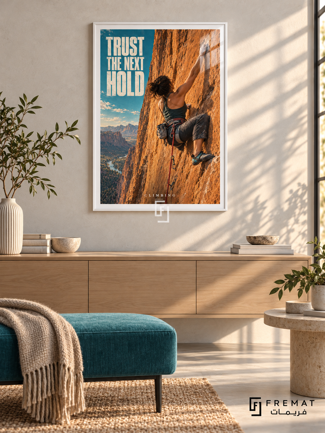 Trust The Next Hold: A climber reaches across an orange rock face, with a red rope and a narrow turquoise sky accent. White frame with a white printed border, displayed in a styled room.